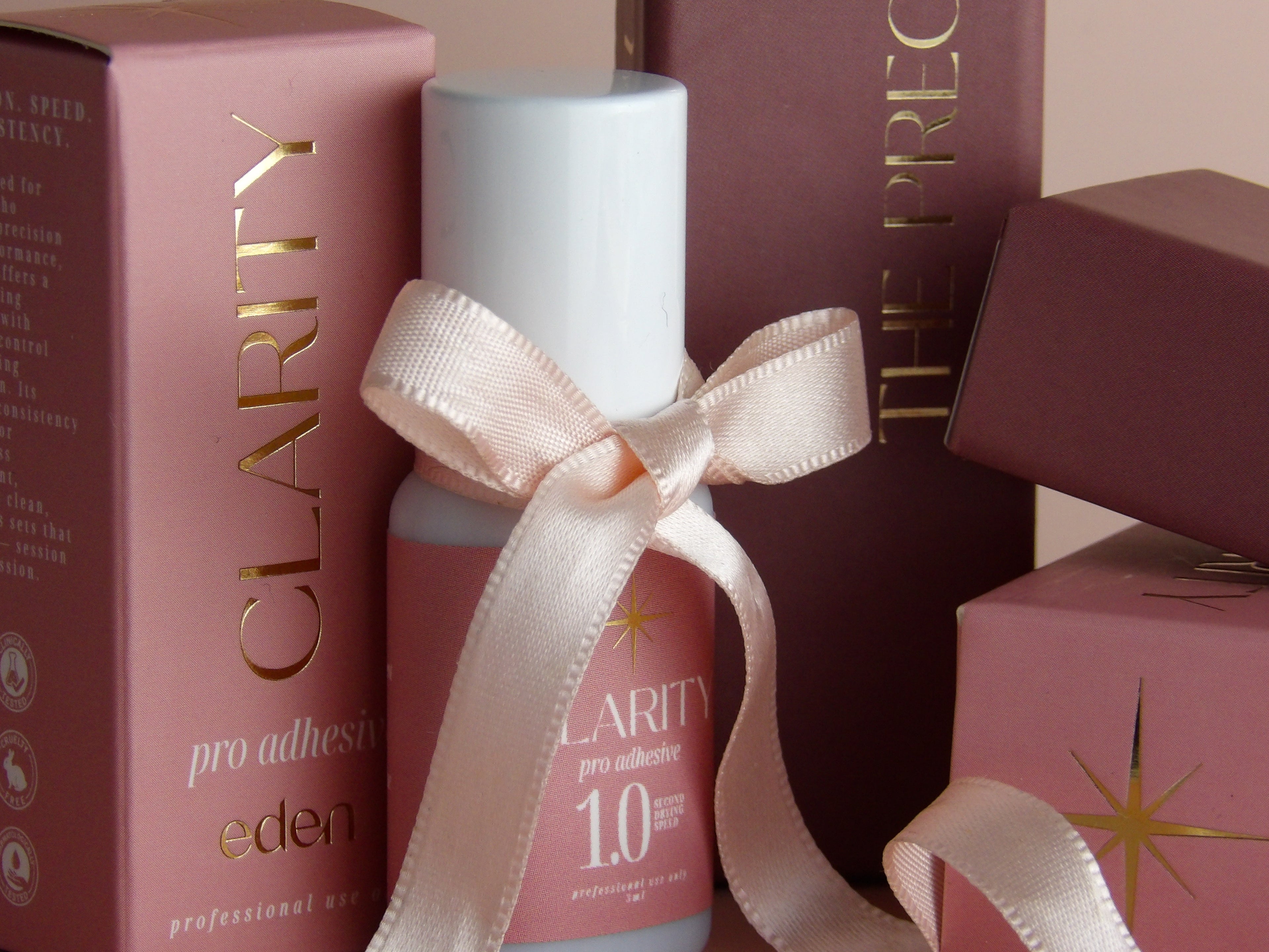 Bottle of Clarity pro adhesive with a pink ribbon against a pink background
