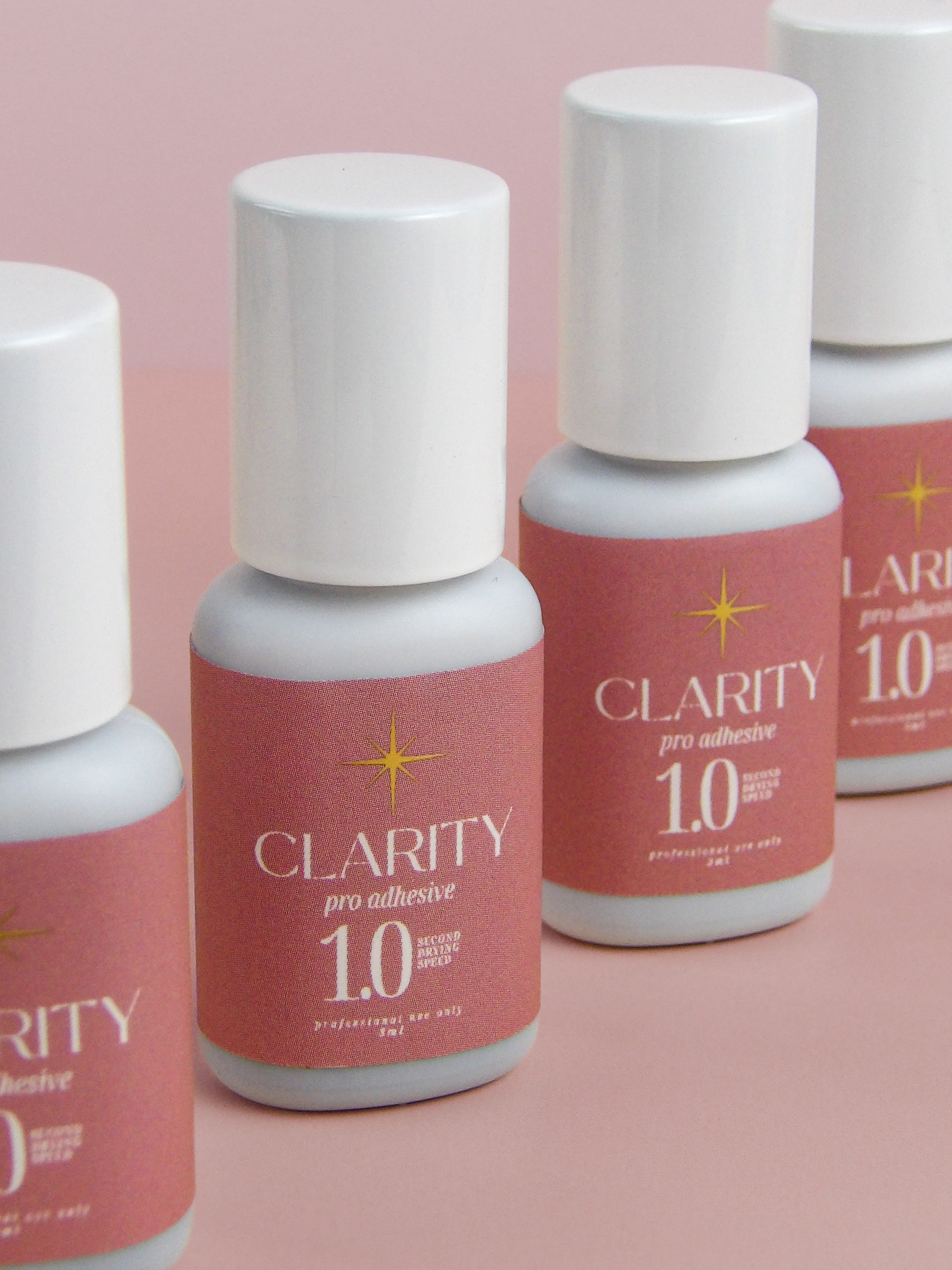 Bottles of Clarity pro adhesive 1.0 on a pink background