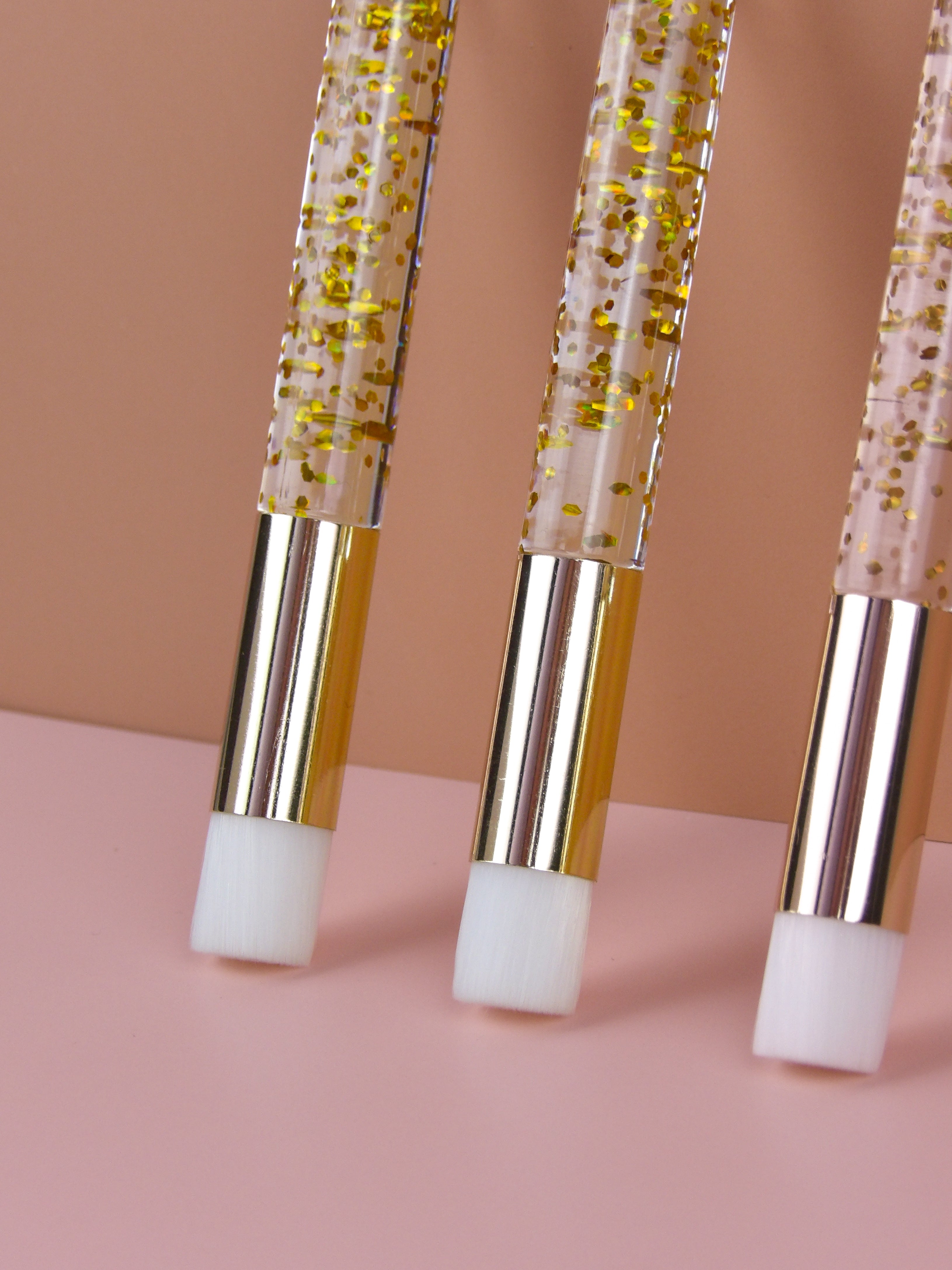 Three cleanse brushes with gold and white accents on a pink background