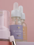 Two bottles of 'Devotion' oil with droppers on a pink background