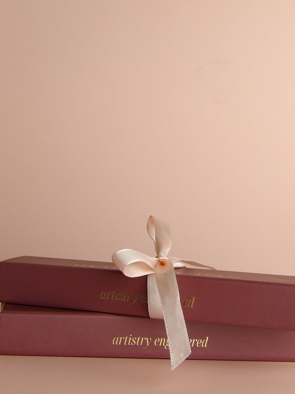Two stacked pink boxes with a white ribbon on a beige background