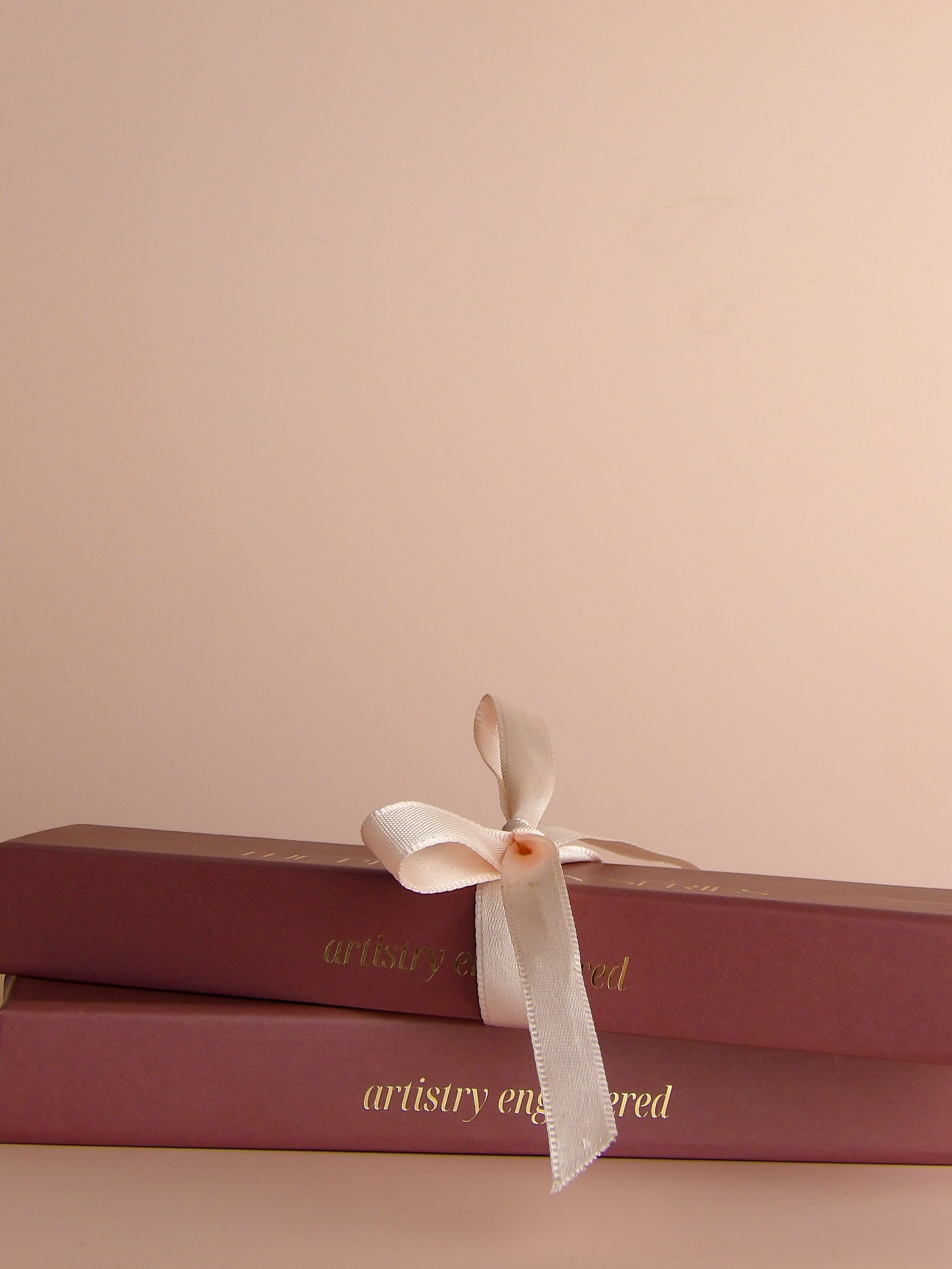 Two stacked pink boxes with a white ribbon on a beige background