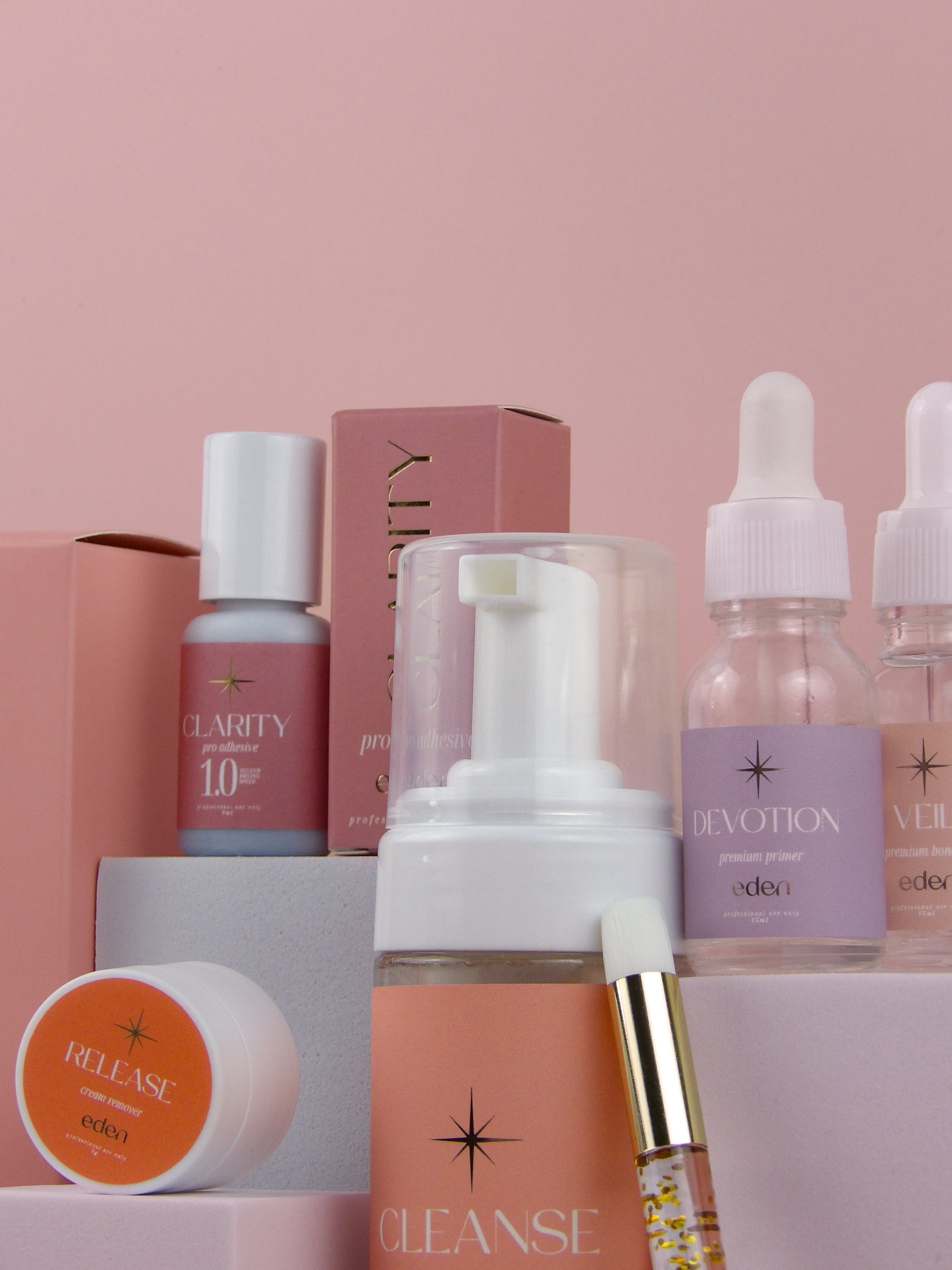Collection of lash products with visible branding on a pink background