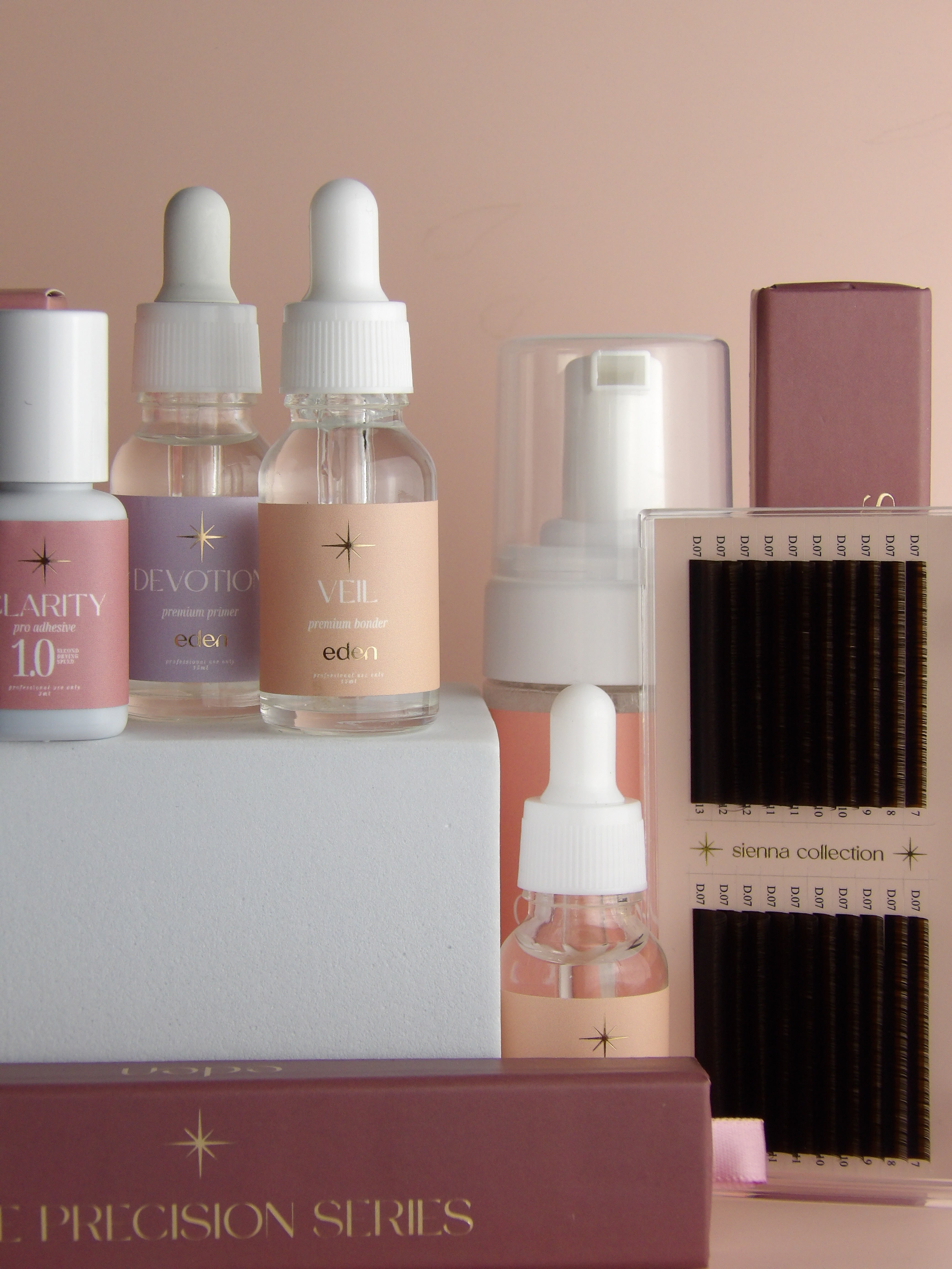 Collection of lash products including bottles and a box on a pink background