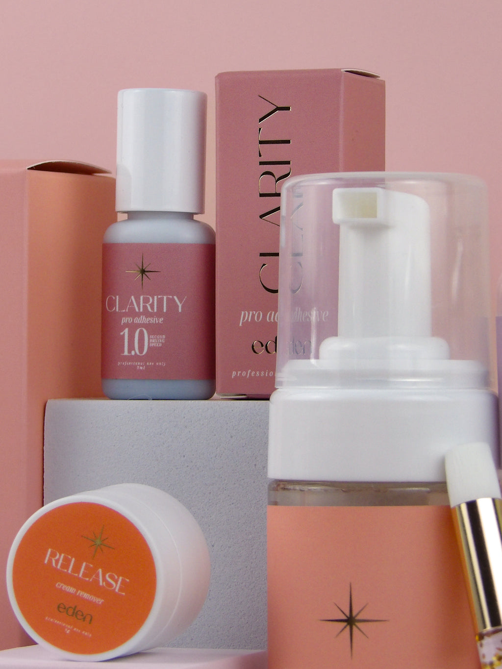 Eden lash products including a bottle, cream, and box on a pink background