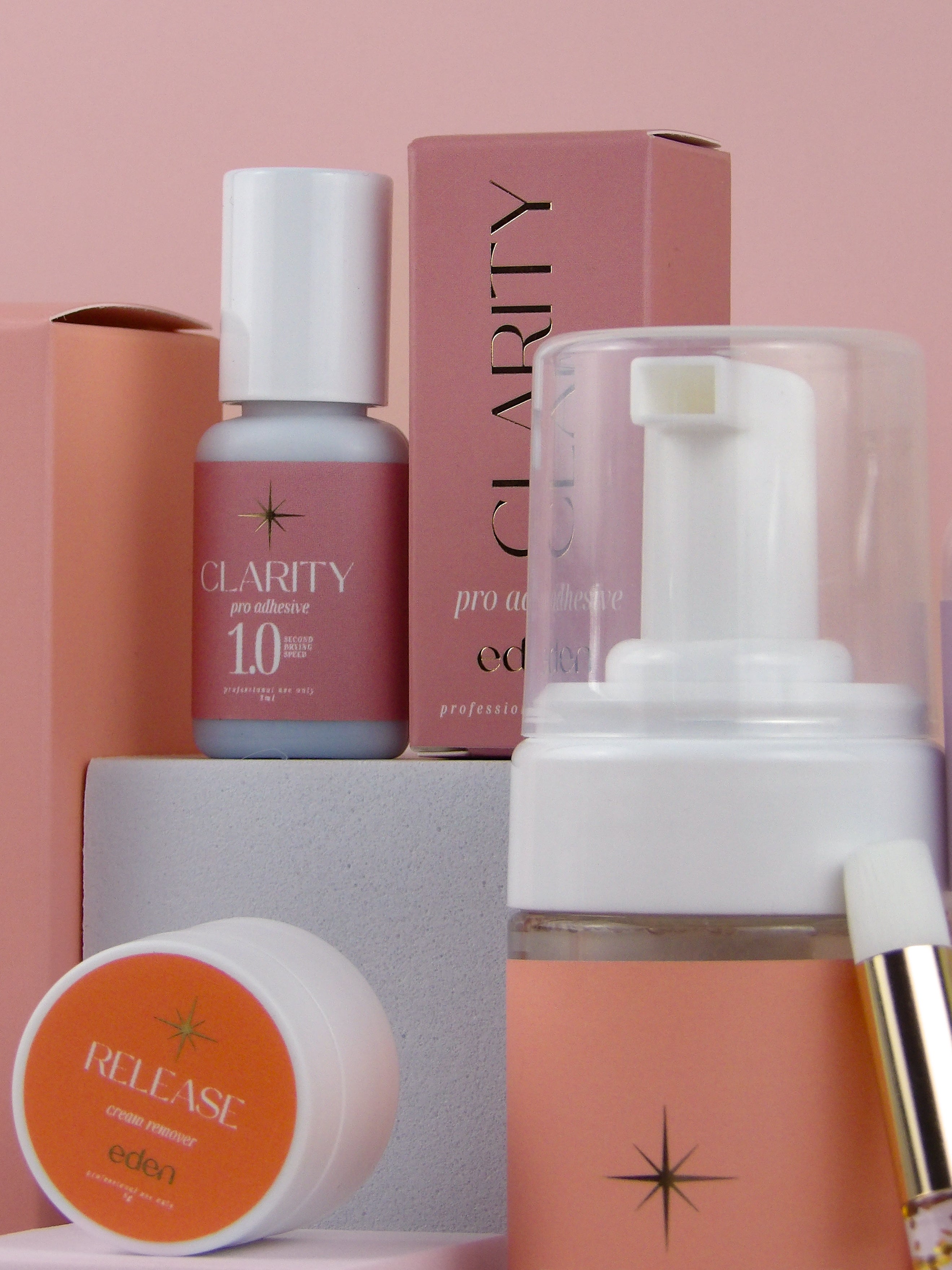 Eden lash products including a bottle, cream, and box on a pink background