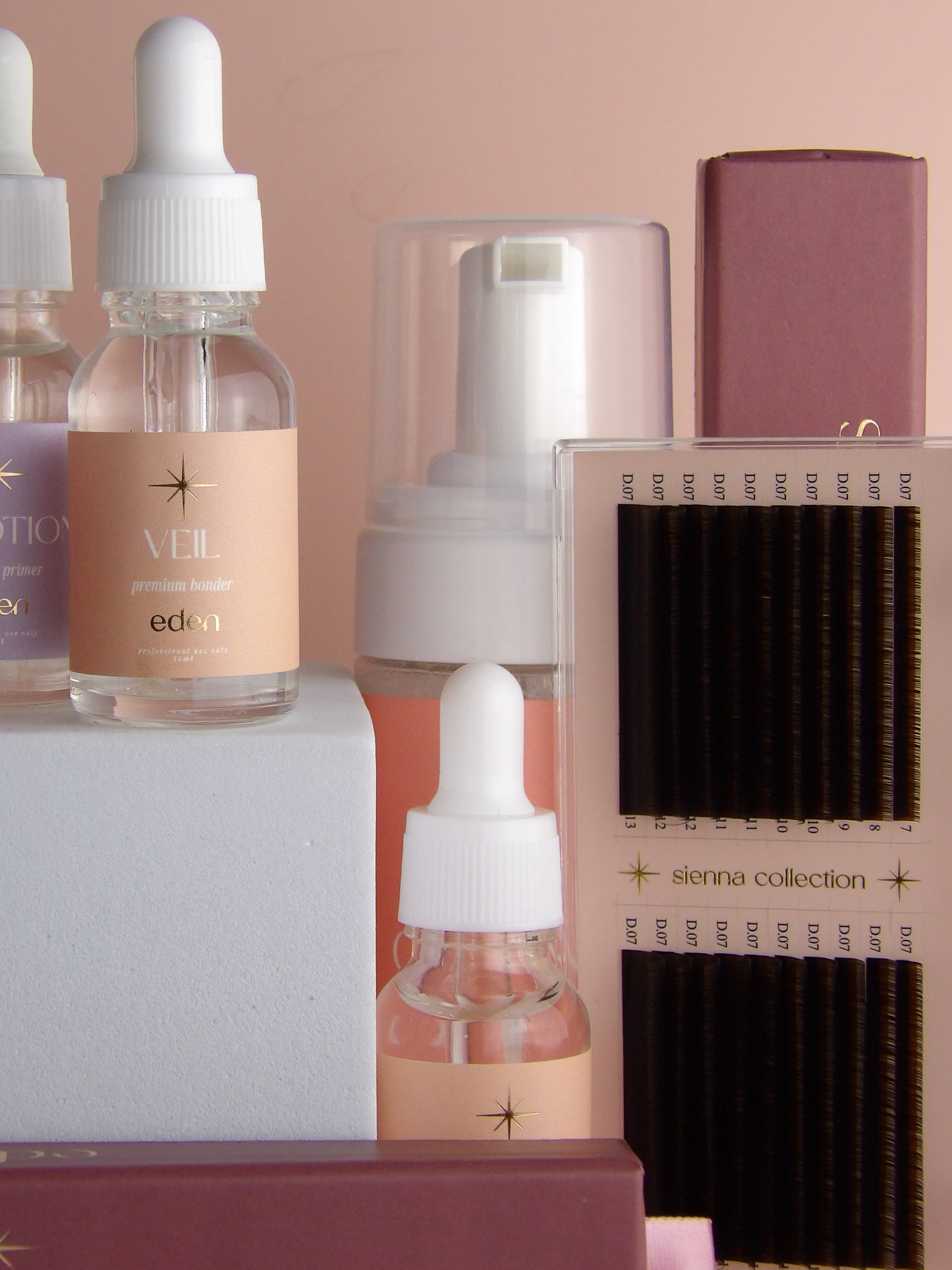 lash products including bottles and a box with eyelash extensions on a neutral background