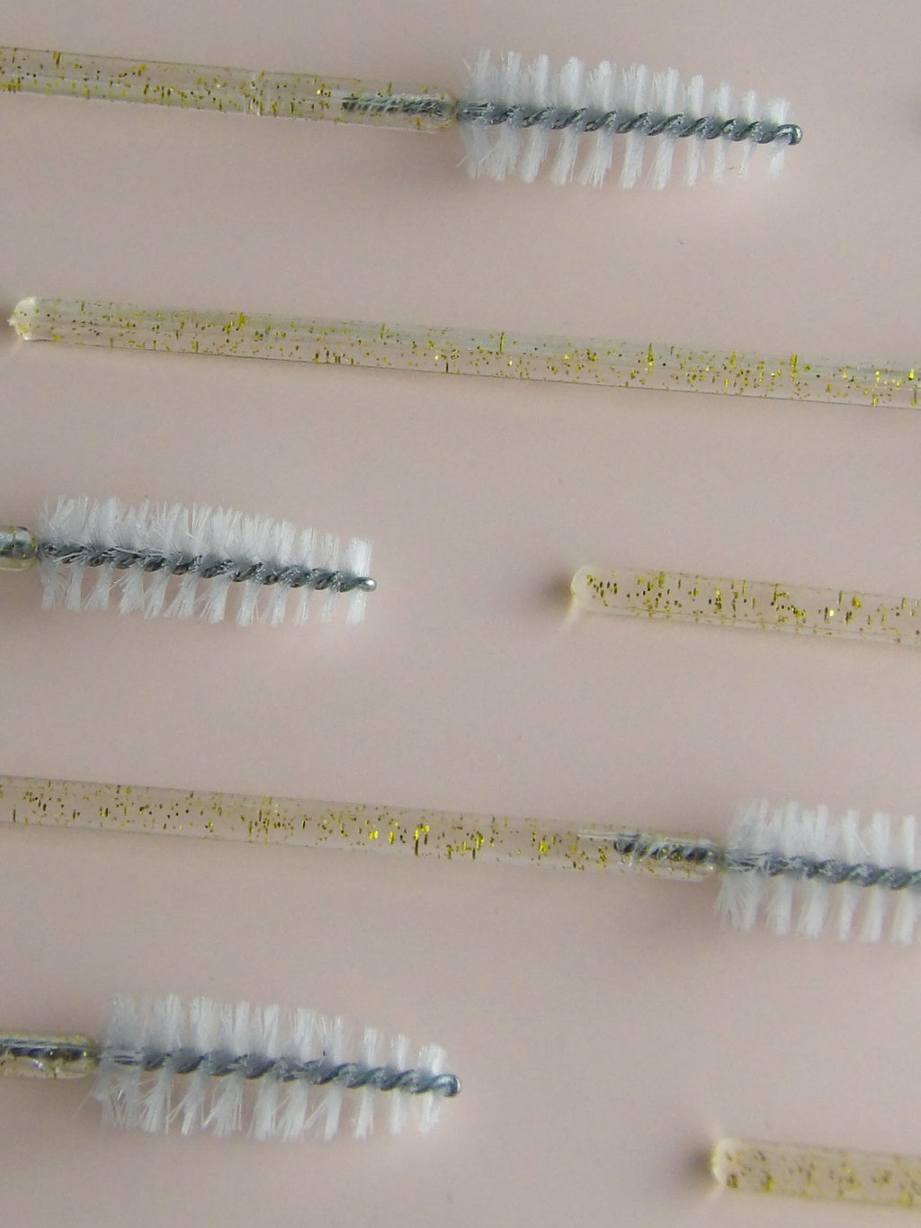 Set of spoolie brushes with different bristle patterns on a beige background