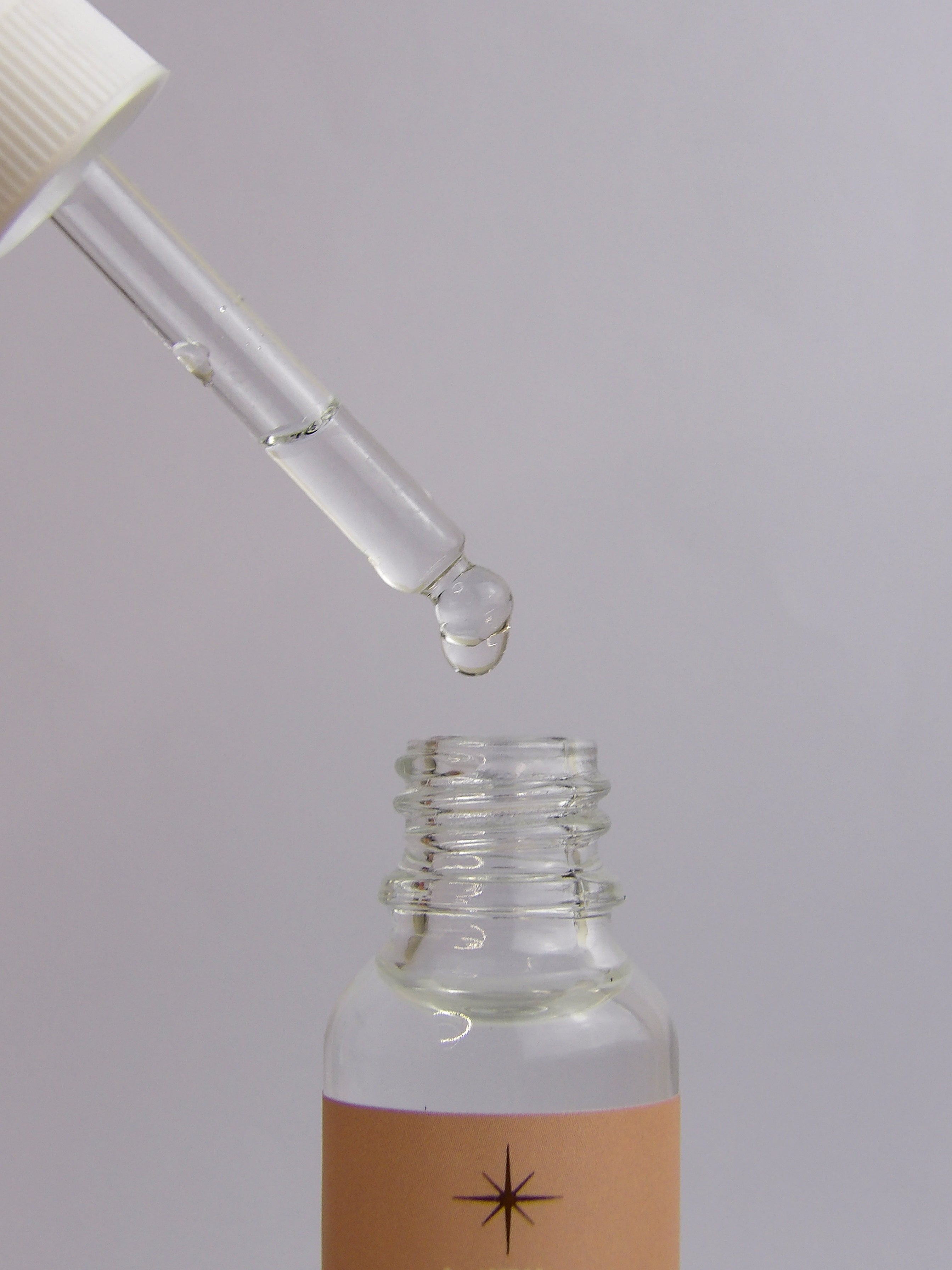Glass dropper bottle with a droplet of liquid on a gray background